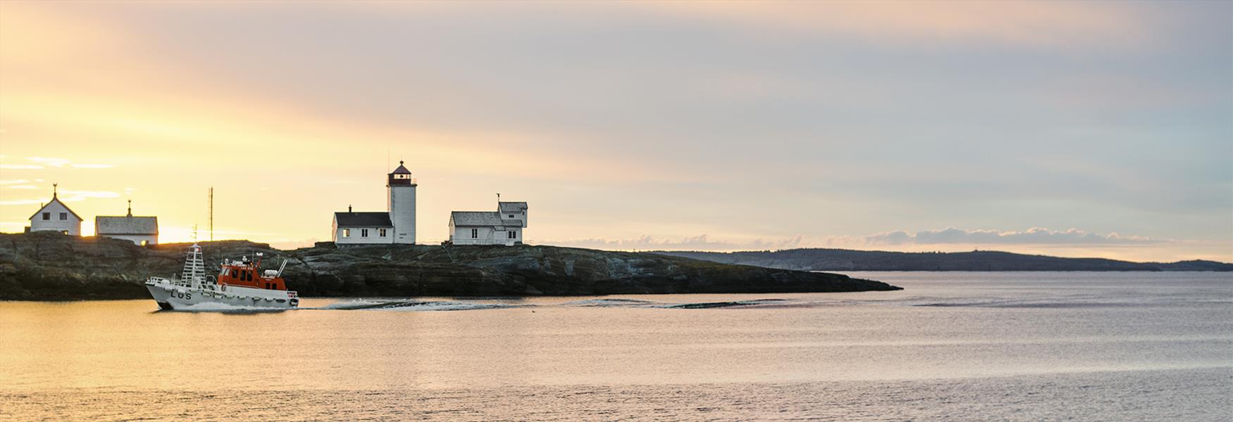 boat drives past Langesund lighthouse at sunset
