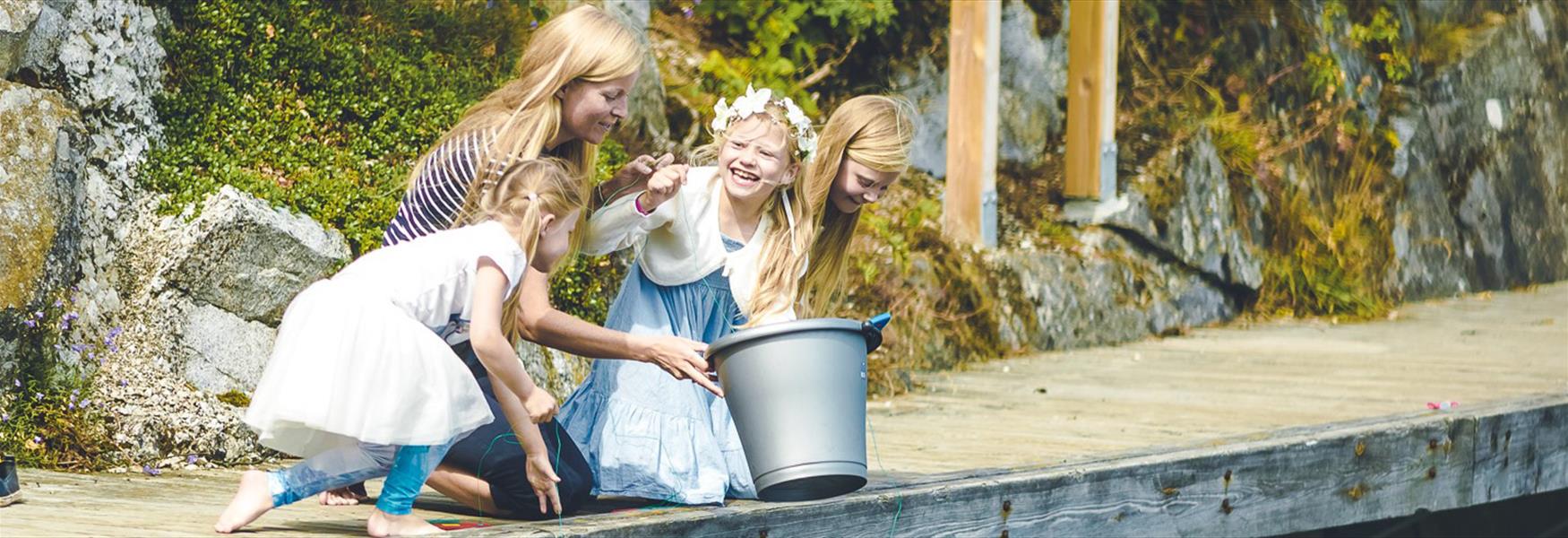 dame med 3 jenter og en bøtte på en brygge
