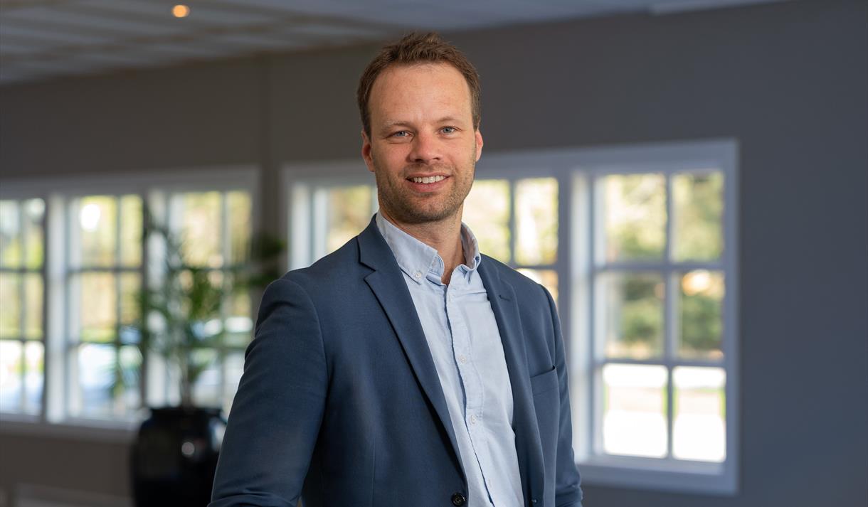 mann med kort mørkt hår, lys blå skjorte og mørk blå jakke