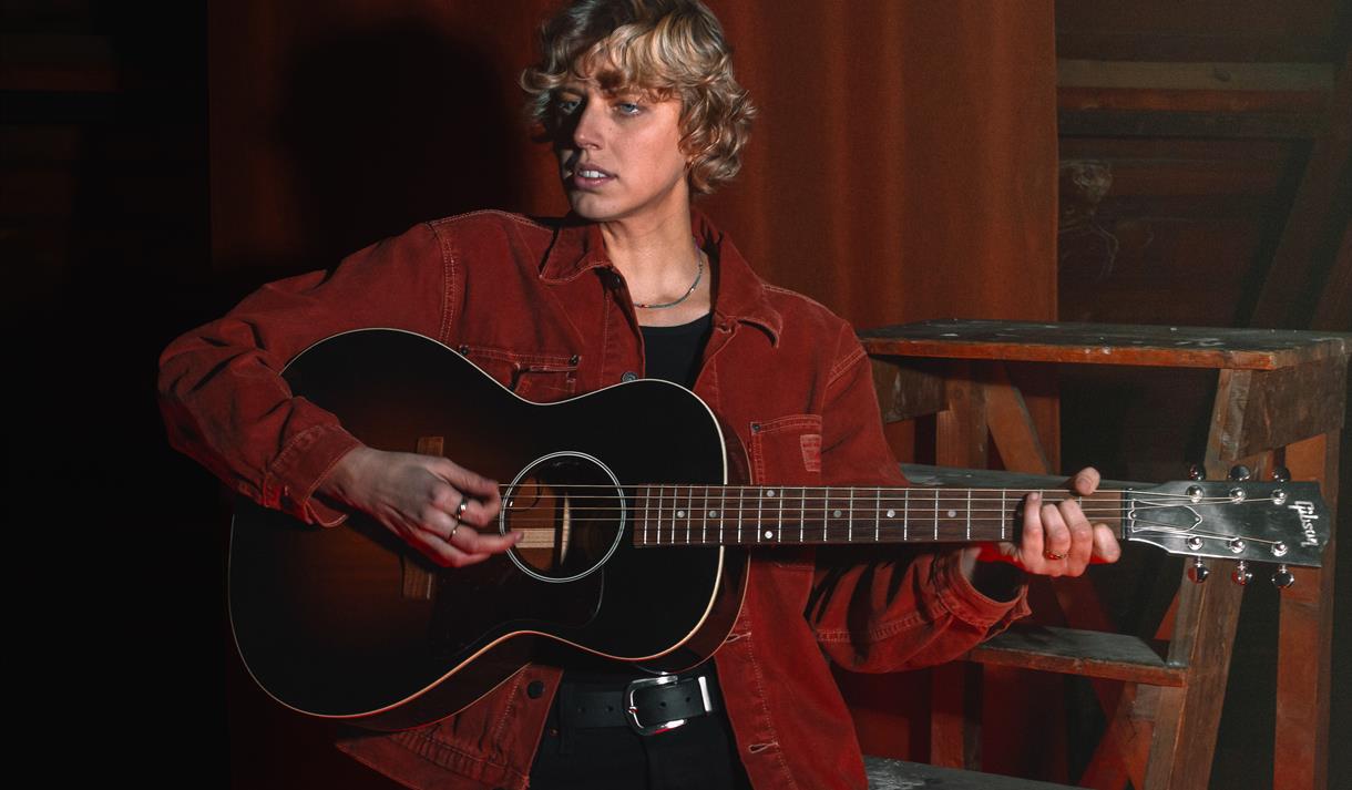 lys dame i rustfargede klær, sort gitar