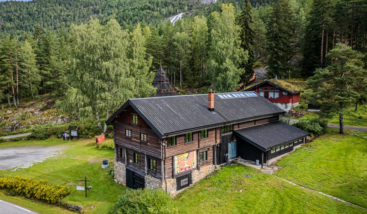 flyfoto av Hillestad galleri, en tømmerbygning omgitt av grønt gress og skog.