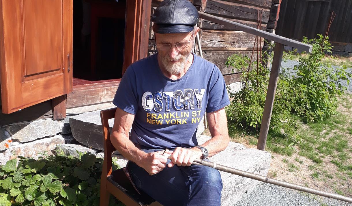 Svein Vinjerui spikkar foran husmannsstoga på Vest-Telemark museum Eidsborg.