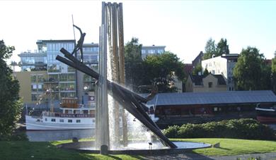 Tømmerfløtermonument i Skien og Hjellebrygge med kanalbåten i bakgrunn