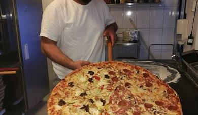 En av My pizza sine ansatte holder stor pizza. Foto