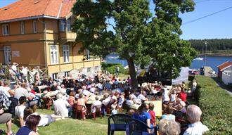 Skougaards hus i Langesund med masse mennesker ute i hagen. Sjøen i bakgrunn.