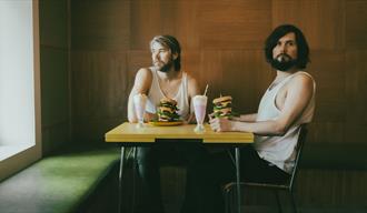 2 menn mede burger og milkshake som sitter på et bord