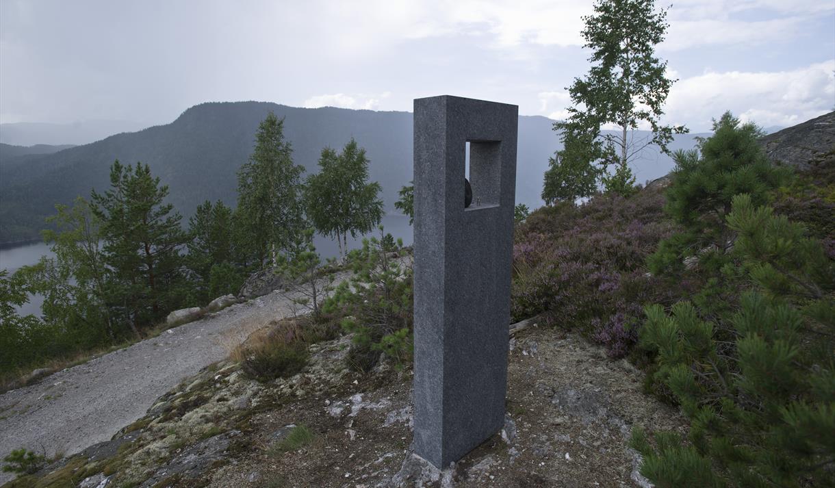 Åtte skulpturelle "kikkeskåp" i stein står ute i landskapet på stader som er knytt til utvalde soger om lokale kvinneskikkelsar. Felles for dei alle er at feleslåttar er knytt til sogene. Åtte kunstnarar har gjeve sine tolkingar av desse sogene: Gonil Dale, Guro Lomodden, Kivlemøyane, Gurp Heddeli, Tårån i troppin, Glima i Rupedalar, Ljose-Signe i Bindingsnuten og Skuldalsbruri.
Du finn 1 kikkeskåp i Åmotsdal, 3 i Flatdal og 4 i Seljord. På alle stadene er det også montert ein benk, der folk kan sitje ned for å nyte ei annleis kunstoppleving i sogelandskapet.
Tanken er å gje ei vakker kunstoppleving, samtidig som dei usynlege laga i landskapet blir formidla gjennom kunstverket, landskapsopplevinga og sogemobilen.
Foto: Dag Jenssen
Kunstnar: Knut Hølje Odden
For å høyre soga og slåtten til , ring sogemobilen på 35 19 76 23, tast 32
