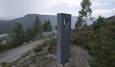Åtte skulpturelle "kikkeskåp" i stein står ute i landskapet på stader som er knytt til utvalde soger om lokale kvinneskikkelsar. Felles for dei alle er at feleslåttar er knytt til sogene. Åtte kunstnarar har gjeve sine tolkingar av desse sogene: Gonil Dale, Guro Lomodden, Kivlemøyane, Gurp Heddeli, Tårån i troppin, Glima i Rupedalar, Ljose-Signe i Bindingsnuten og Skuldalsbruri.
Du finn 1 kikkeskåp i Åmotsdal, 3 i Flatdal og 4 i Seljord. På alle stadene er det også montert ein benk, der folk kan sitje ned for å nyte ei annleis kunstoppleving i sogelandskapet.
Tanken er å gje ei vakker kunstoppleving, samtidig som dei usynlege laga i landskapet blir formidla gjennom kunstverket, landskapsopplevinga og sogemobilen.
Foto: Dag Jenssen
Kunstnar: Knut Hølje Odden
For å høyre soga og slåtten til , ring sogemobilen på 35 19 76 23, tast 32
