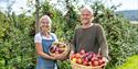 eldre par står foran frukttrær med fruktkurv i hendene