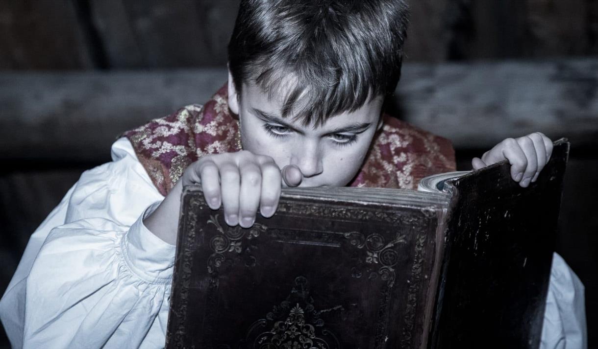 en liten gutt i gamledagse klær som leser i en stor gammel bok