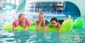 3 barn som ligger på en luftmadrass i bassenget til badeparken