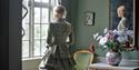 dame i en pen kjole står ved vinduet i et staselig rom på Brekkeparken