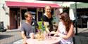 En servitør fra Cafe Felicia serverer to gjester på uteserveringen, i Notodden. Foto