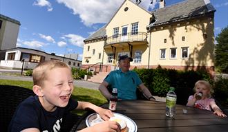 Familie koser seg på uteserveringen til Stasjonen Kafé i hydroparken, i Notodden en sommerdag. Foto